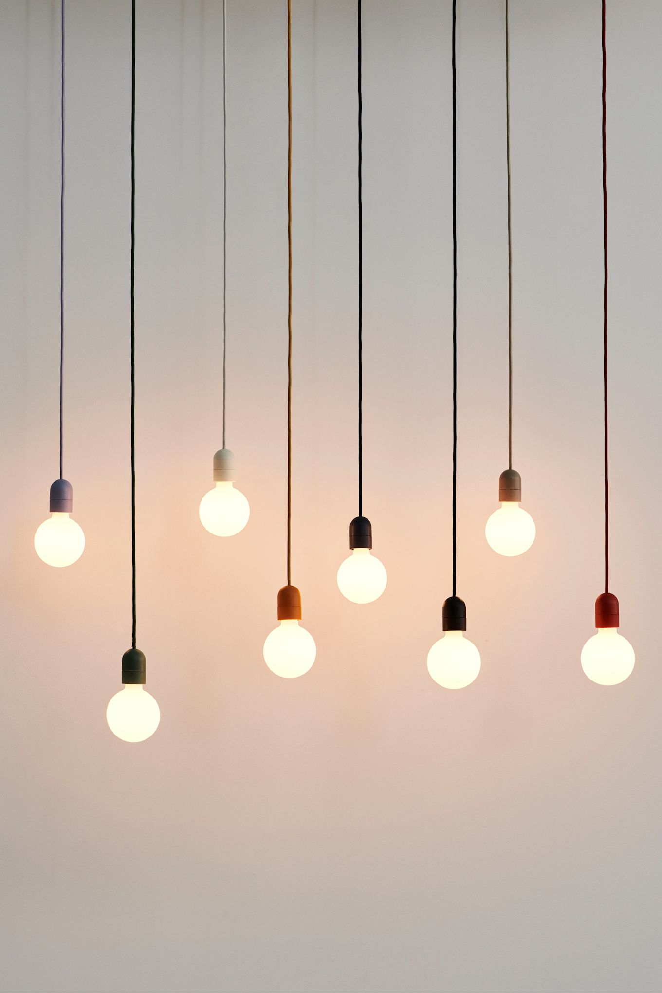 The Muuto E27 lamps hanging in a collection with multi coloured cables. 