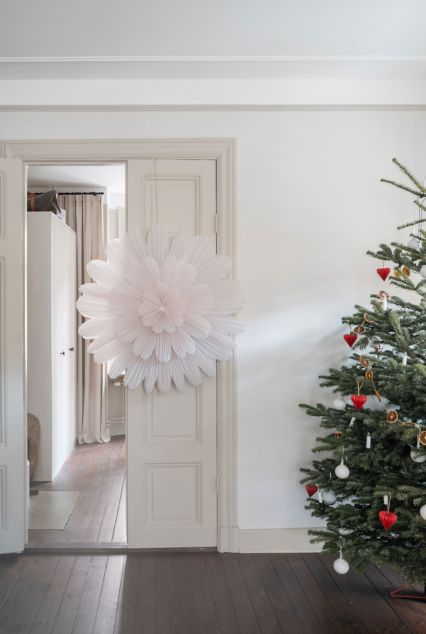 Pappersstjärnlyktan Snöblomma från Watt & Veke i en enorm storlek på 100 cm hänger i dörröppningen till ett vardagsrum bredvid en julgran. 