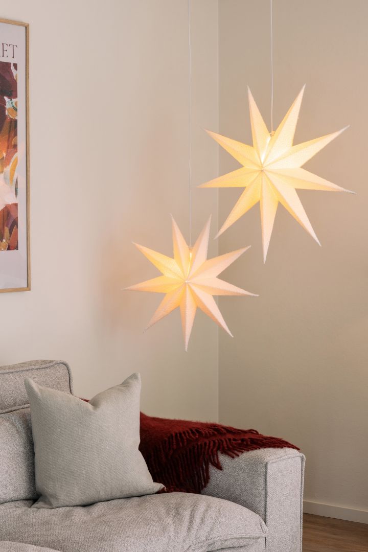 Die Papiersterne Stella Boucle von Globen Lighting hängen in einem Paar in einem Wohnzimmer über einem Sofa. 